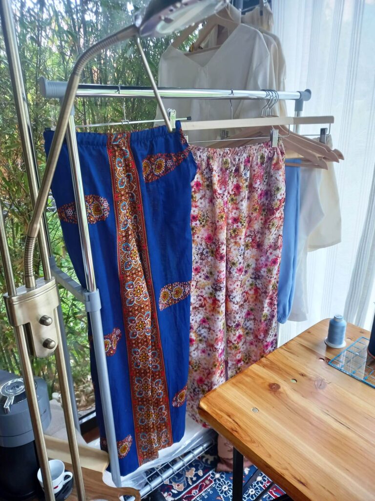 telas africanas colgadas en percheros en la tienda hkane y plantas verdes al fondo